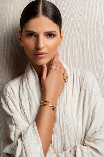 A woman wearing a gold diamond wrap bangle bracelet set with malachite and luxury earrings